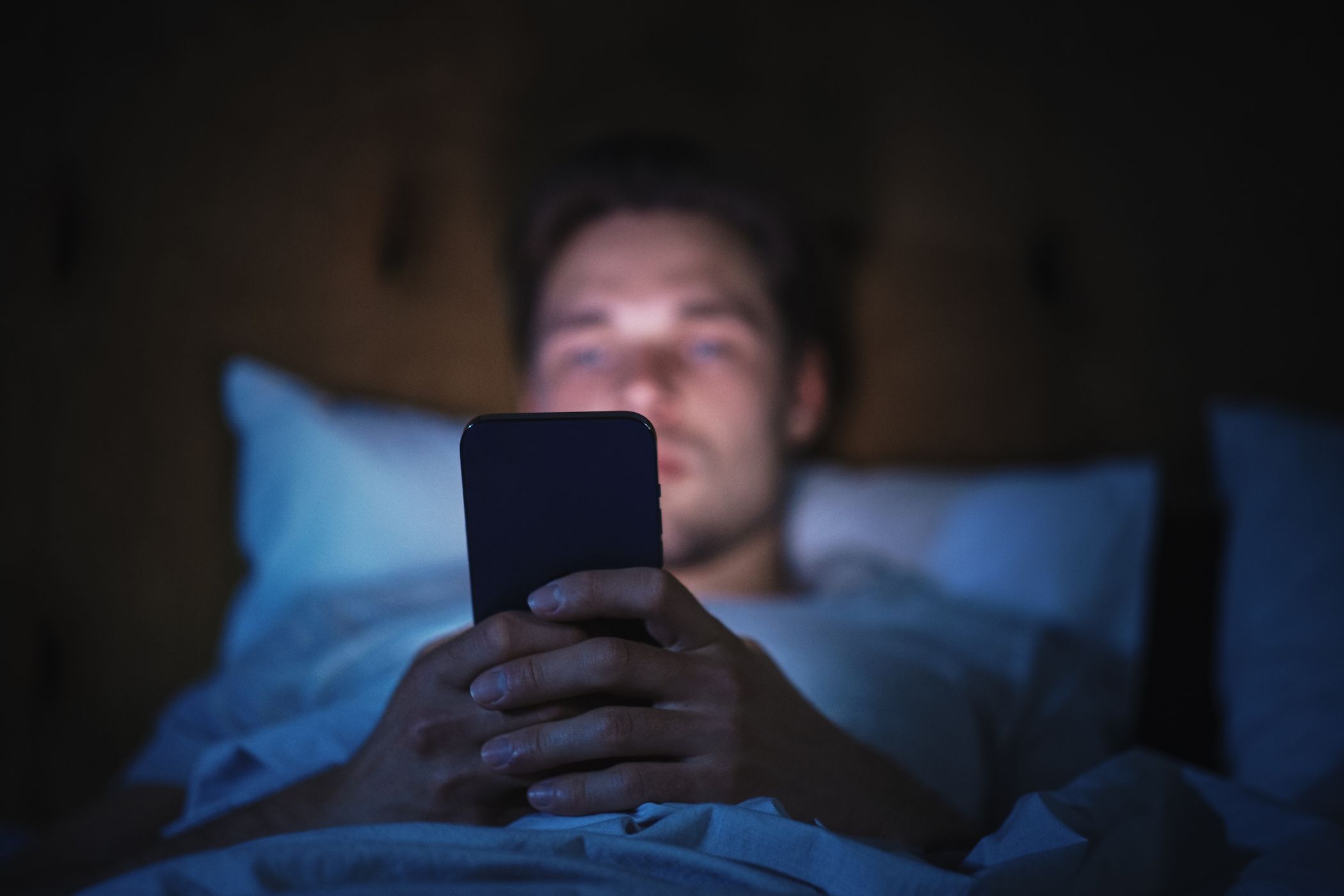 A man using a smartphone while lying in bed